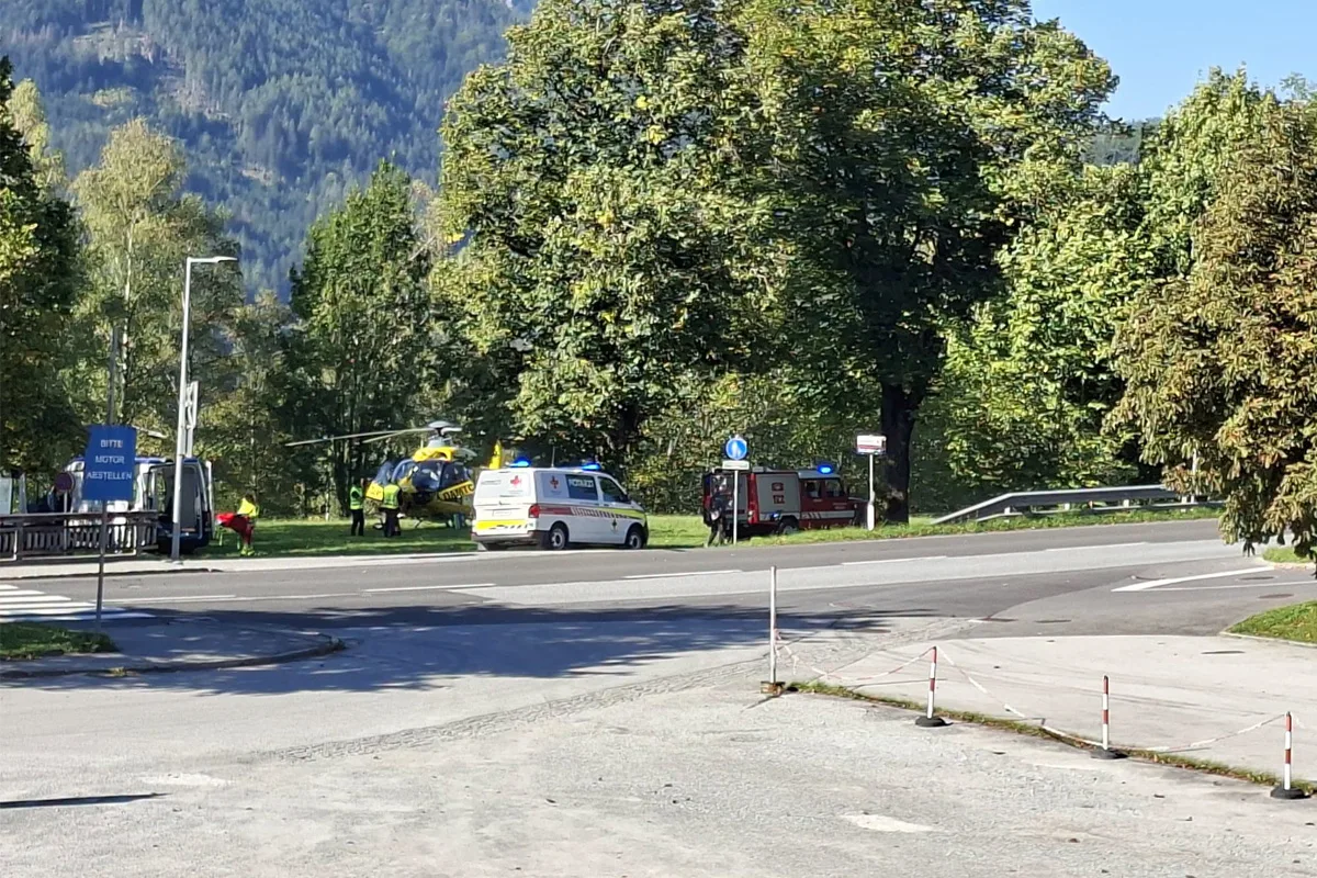 Ein gelber Rettungshubschrauber steht auf einer Wiese neben einer Straße, daneben steht ein Ambulanzfahrzeug.