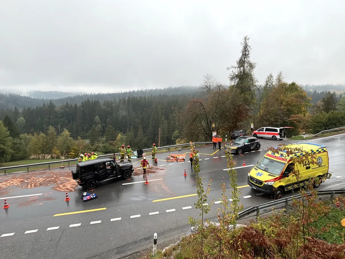 Ein Unfall auf einer Landstraße zeigt Einsatzfahrzeuge und Rettungskräfte, die die Szene sichern. Der Hintergrund ist ein bewaldetes Gebiet.