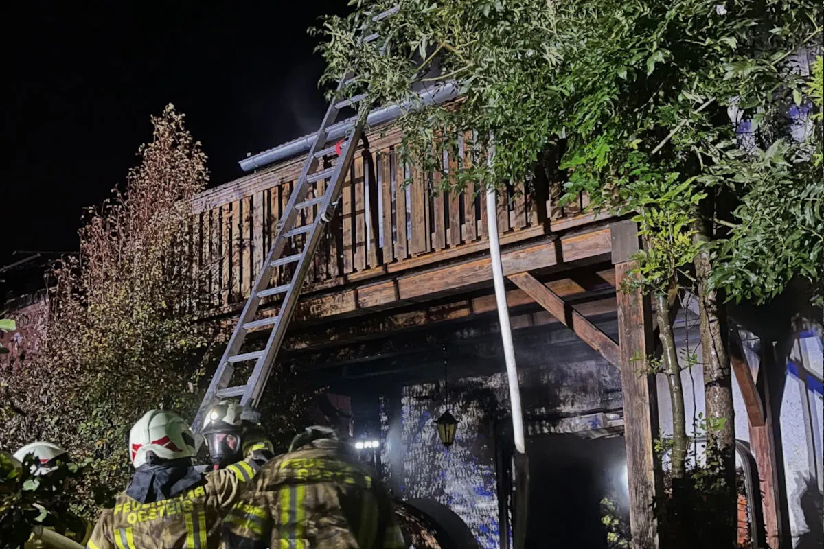 Mehrere Feuerwehrleute stehen bei einem nächtlichen Einsatz vor einem Gebäude mit Holzterrasse und Leiter.