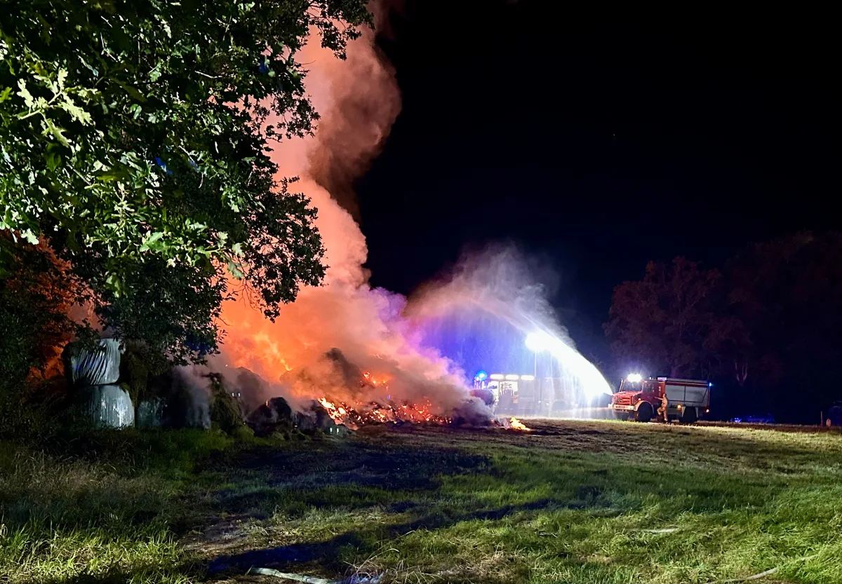 In der Nacht wird ein Feuer auf einem Feld von der Feuerwehr gelöscht. Flammen und Rauch sind deutlich sichtbar.