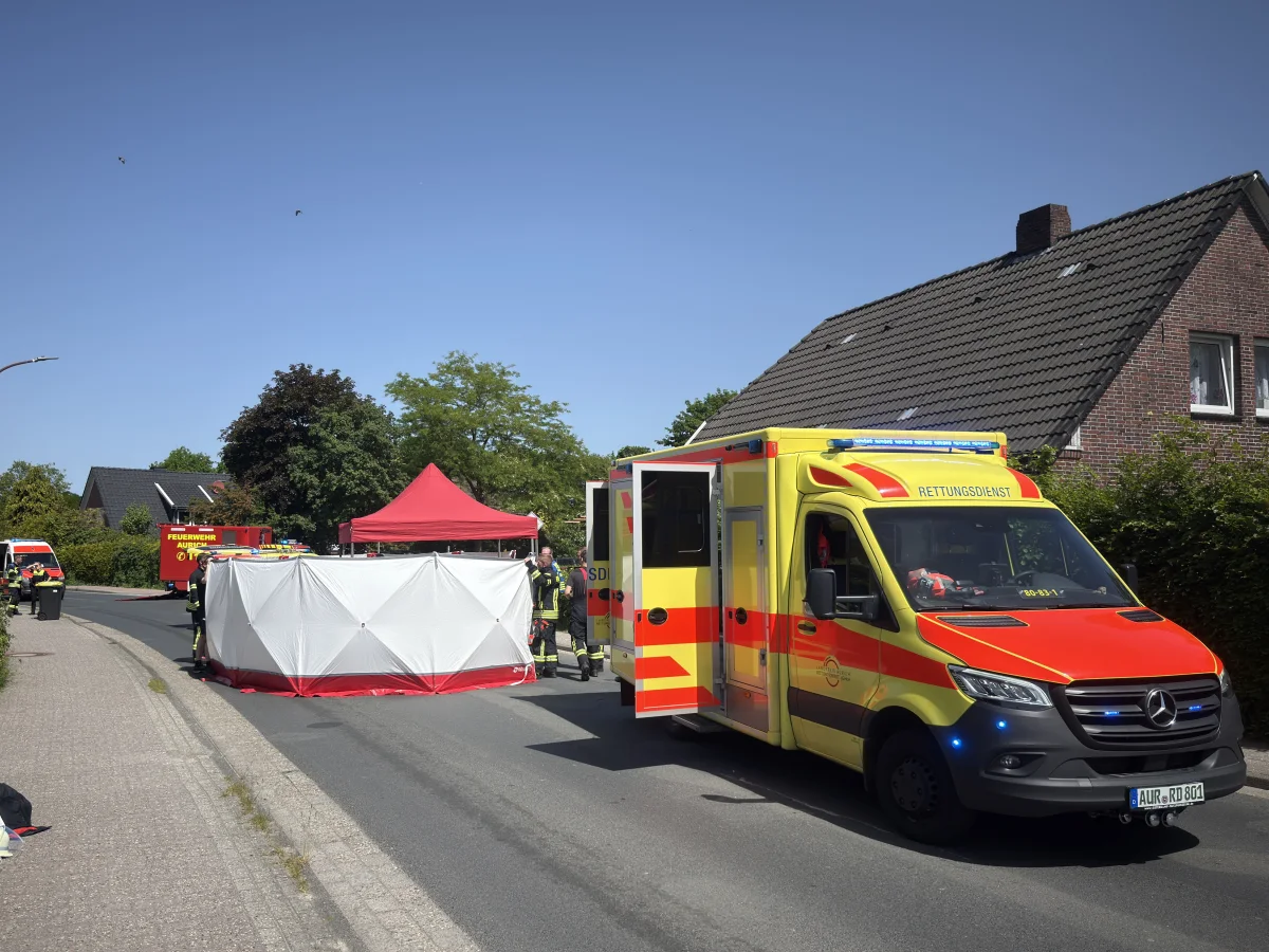 Ein Rettungswagen steht in einer Wohnstraße, flankiert von einer weißen Sichtschutzwand und einem roten Zelt.