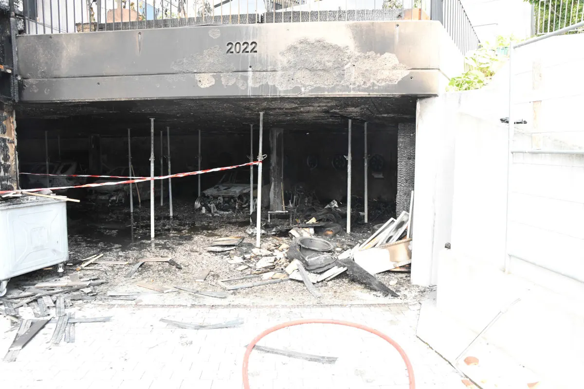 Es ist eine zerstörte und ausgebrannte Tiefgarage zu sehen, in der Reste von Fahrzeugen und Trümmern auf dem Boden liegen. Die Wände und Decke sind von Ruß geschwärzt.