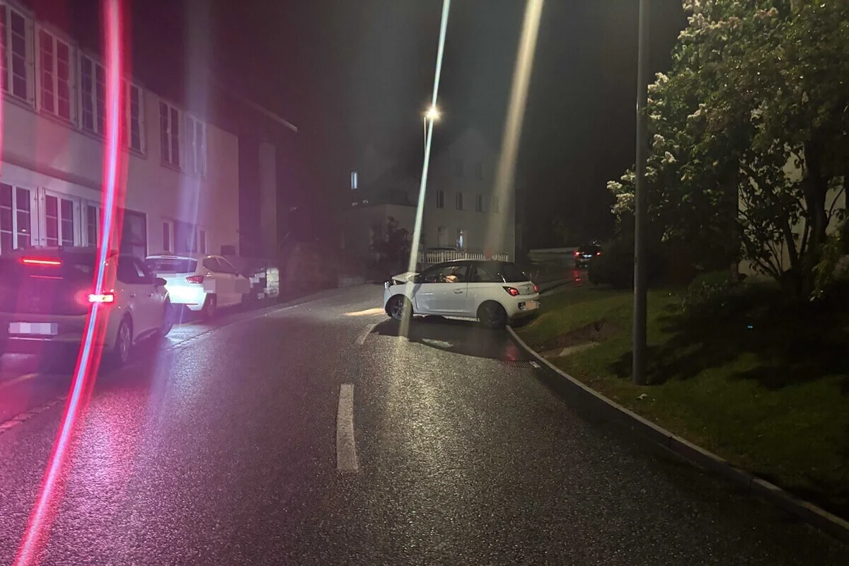 Mehrere Autos stehen am Rand einer nassen, nachts beleuchteten Straße. Ein weißes Auto steht quer auf der Fahrbahn.