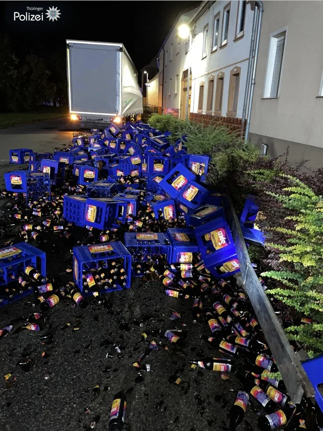 Ein Lkw steht auf einer nächtlichen Straße, umgeben von zahlreichen umgekippten und beschädigten Bierkisten.