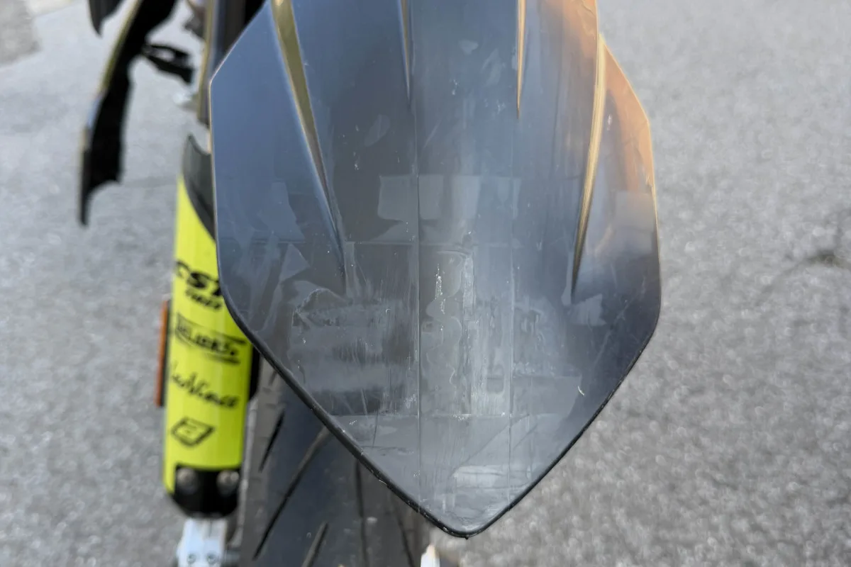 Ein Motorrad von hinten, fokussiert auf das schmutzige Schutzblech und den Hinterreifen, steht auf einer Straße.