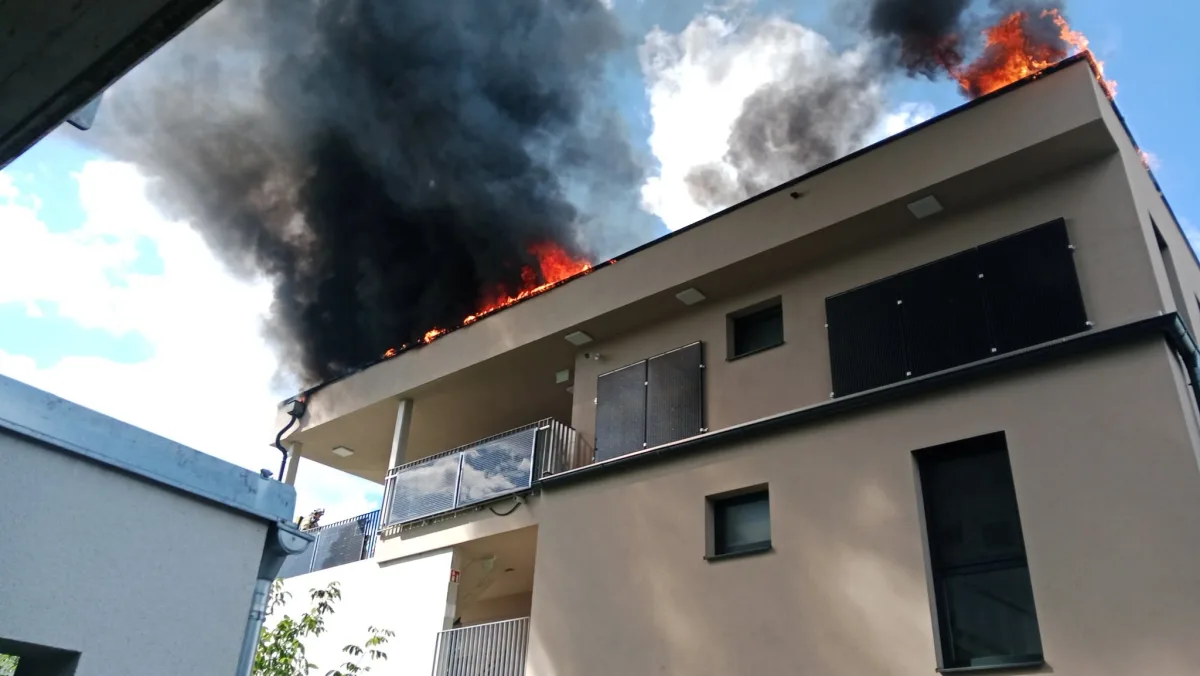 Ein modernes Wohnhaus mit Feuer und starkem Rauch am Dach. Der Himmel ist teils bewölkt.