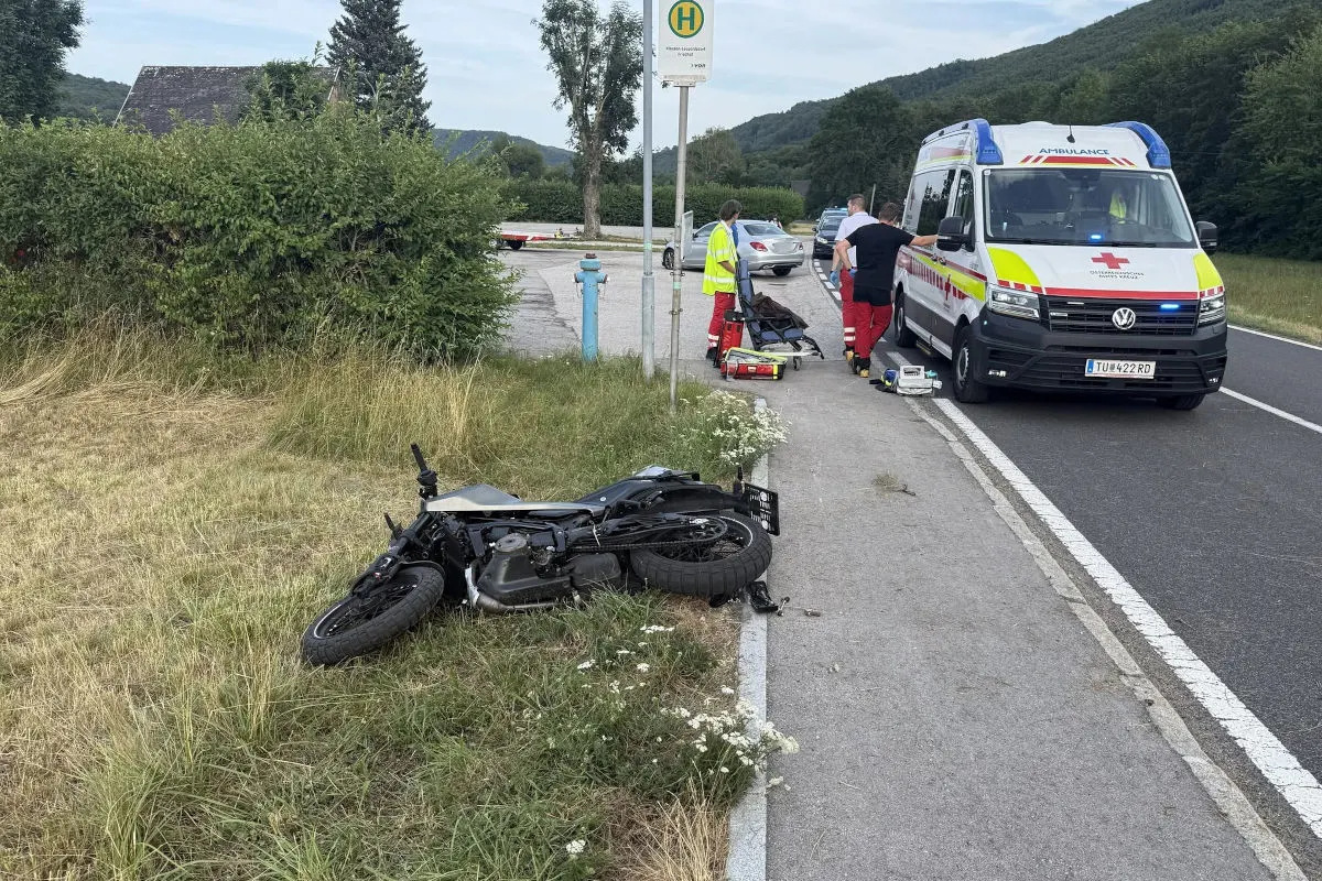 Ein Motorrad liegt auf einer Wiese nahe der Straße, während Rettungskräfte bei einem Krankenwagen stehen.