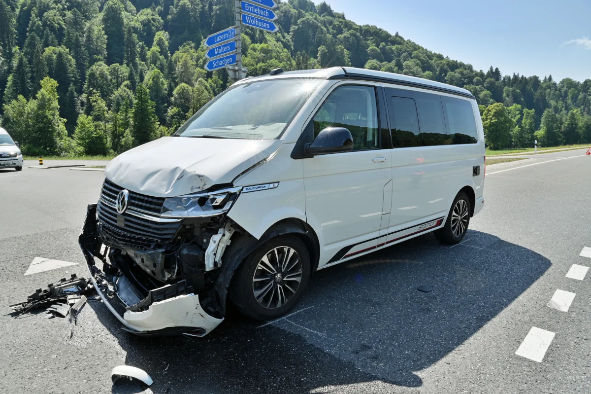 Ein weißer VW-Transporter mit beschädigter Front steht an einer Kreuzung, umgeben von Straßenschildern im Grünen.