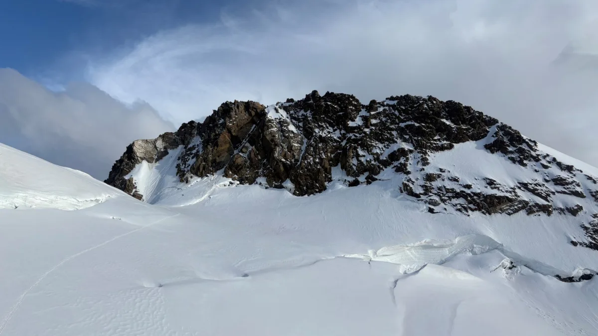 Ein verschneiter Berggipfel erhebt sich unter einem teils bewölkten blauen Himmel. Der Gletscher zieht sich über das Bild.