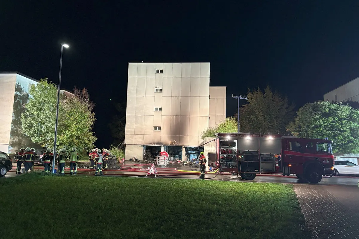 Bei Nacht bekämpft die Feuerwehr einen Brand im Erdgeschoss eines Mehrfamilienhauses. Mehrere Feuerwehrleute und ein Löschfahrzeug sind im Einsatz.