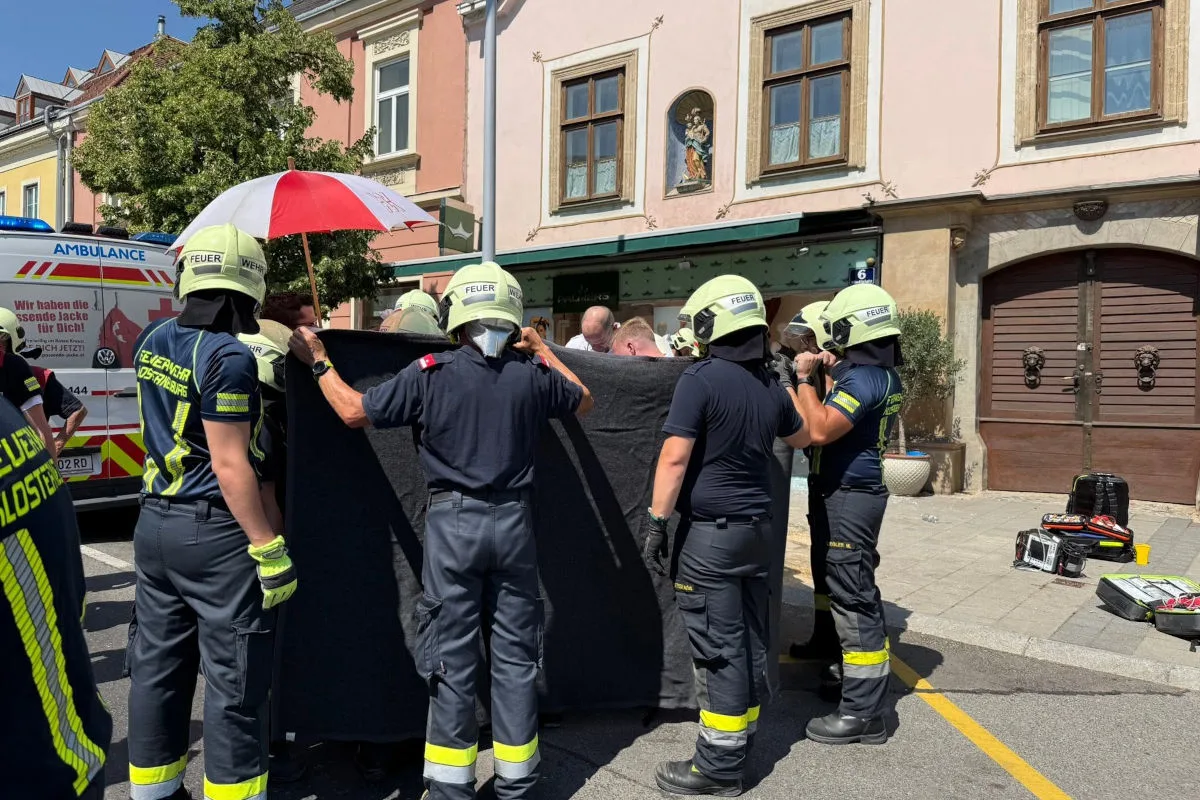 Mehrere Feuerwehrleute in Einsatzkleidung schirmen einen Bereich mit einem Tuch ab. Ein Krankenwagen steht in der Nähe.