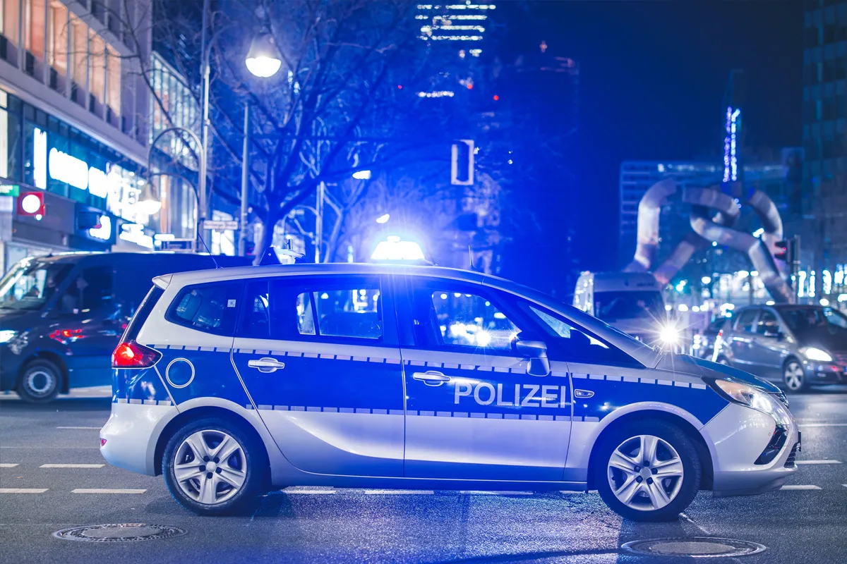 Ein Polizeiauto mit der Aufschrift 'Polizei' ist bei Nacht im Stadtgebiet zu sehen. Es hat das Blaulicht eingeschaltet und steht an einer Kreuzung.