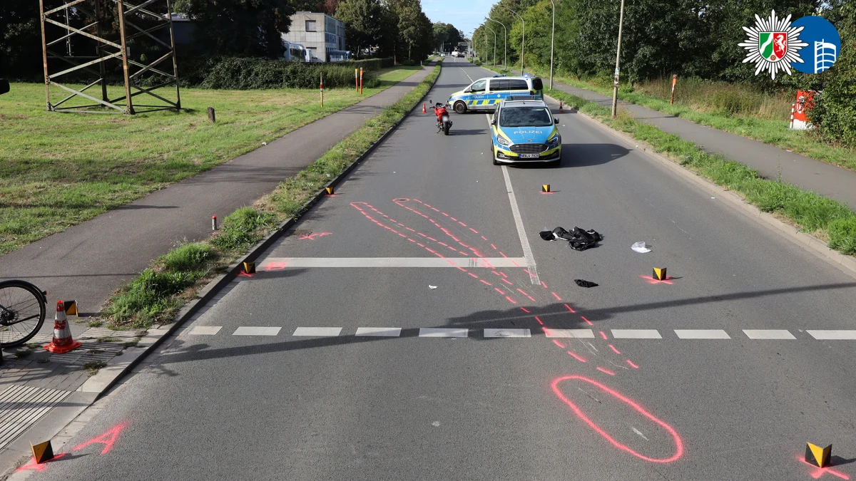 Eine Landstraße mit einem Polizeiauto, einem Motorrad und pinken Markierungen, die einen Unfallort kennzeichnen.