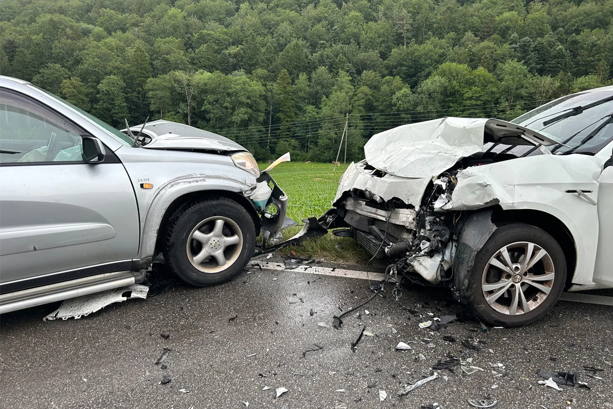 Zwei stark beschädigte Fahrzeuge sind nach einem Frontalzusammenstoß auf einer Landstraße zu sehen. Der Aufprall hat beide Autohecks stark verformt, wobei Trümmerteile auf der Straße verstreut liegen.