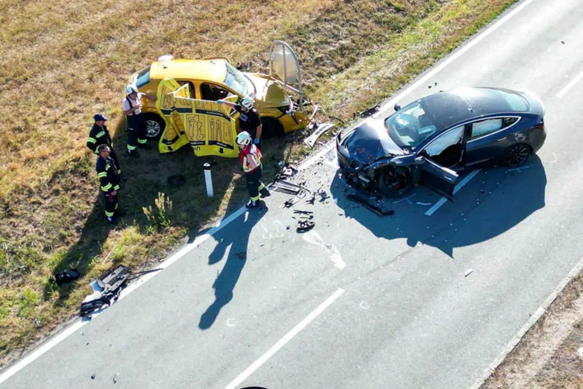 Ein gelbes und ein schwarzes Fahrzeug sind nach einem Unfall beschädigt. Einsatzkräfte in Uniformen sind vor Ort und inspizieren den Schaden.