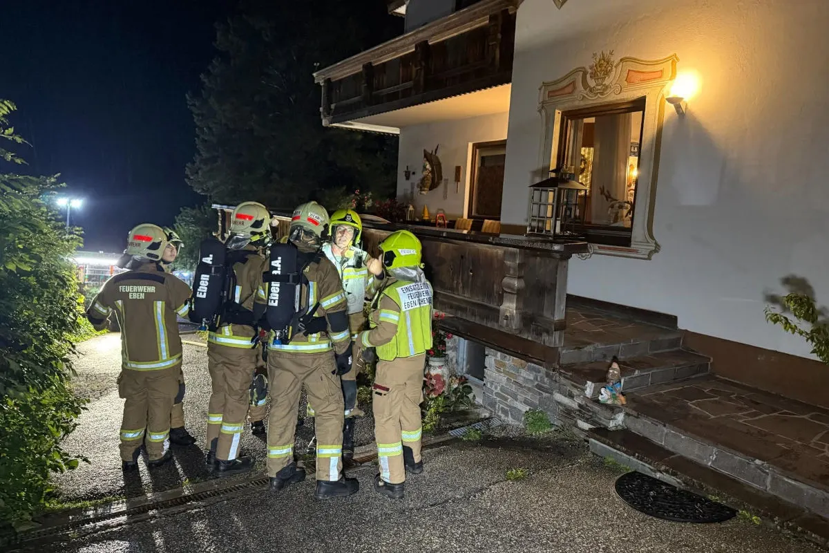 Mehrere Feuerwehrmänner in Einsatzkleidung stehen nachts vor einem beleuchteten Gebäude mit Holzveranda.