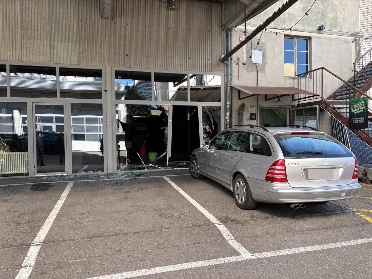Ein grauer Mercedes C200 ist durch ein Schaufenster in ein Gebäude gefahren. Glasscherben liegen vor der beschädigten Front.