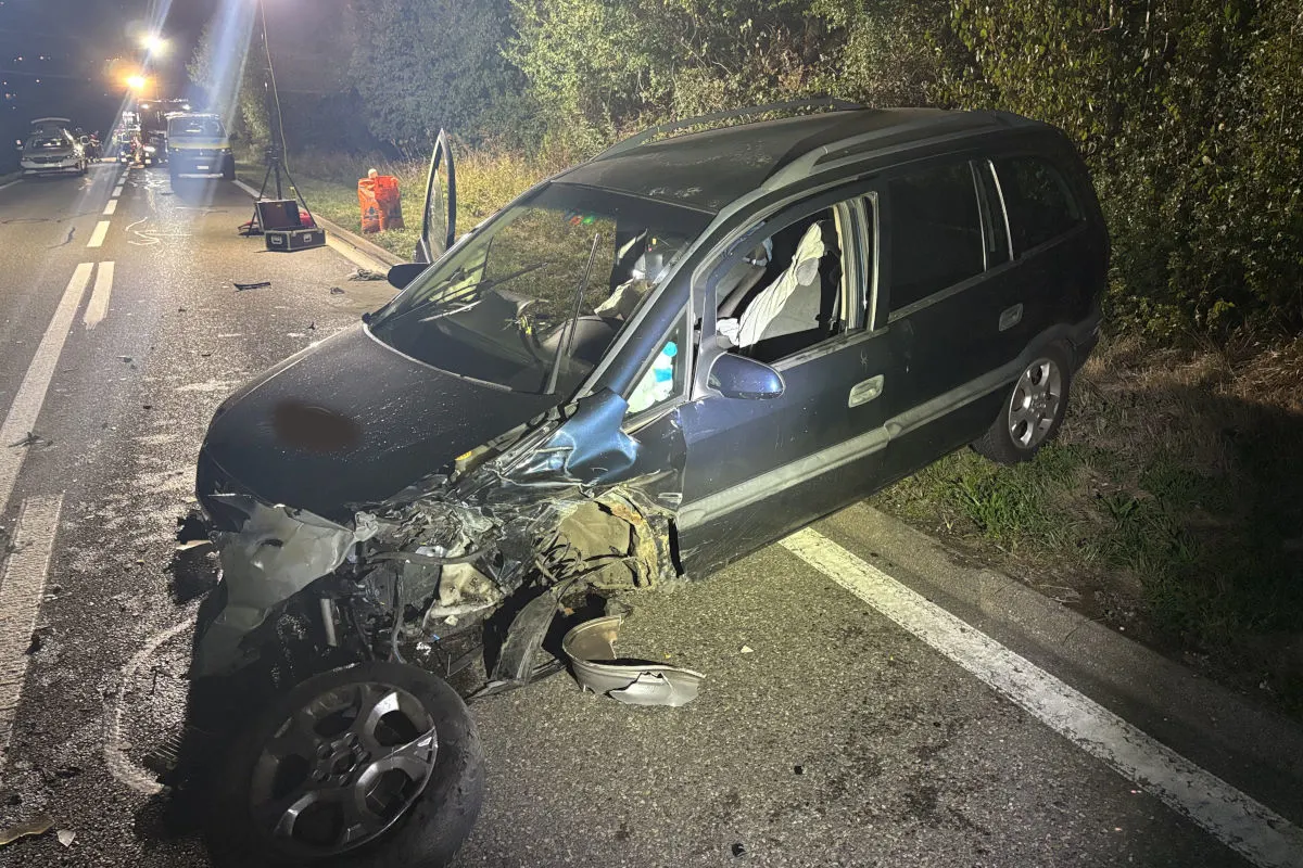 Ein schwer beschädigter blauer Pkw steht auf einer Landstraße, der vordere Teil ist eingedrückt, und der Airbag ist ausgelöst. Im Hintergrund sind Einsatzfahrzeuge und Flutlichter sichtbar.