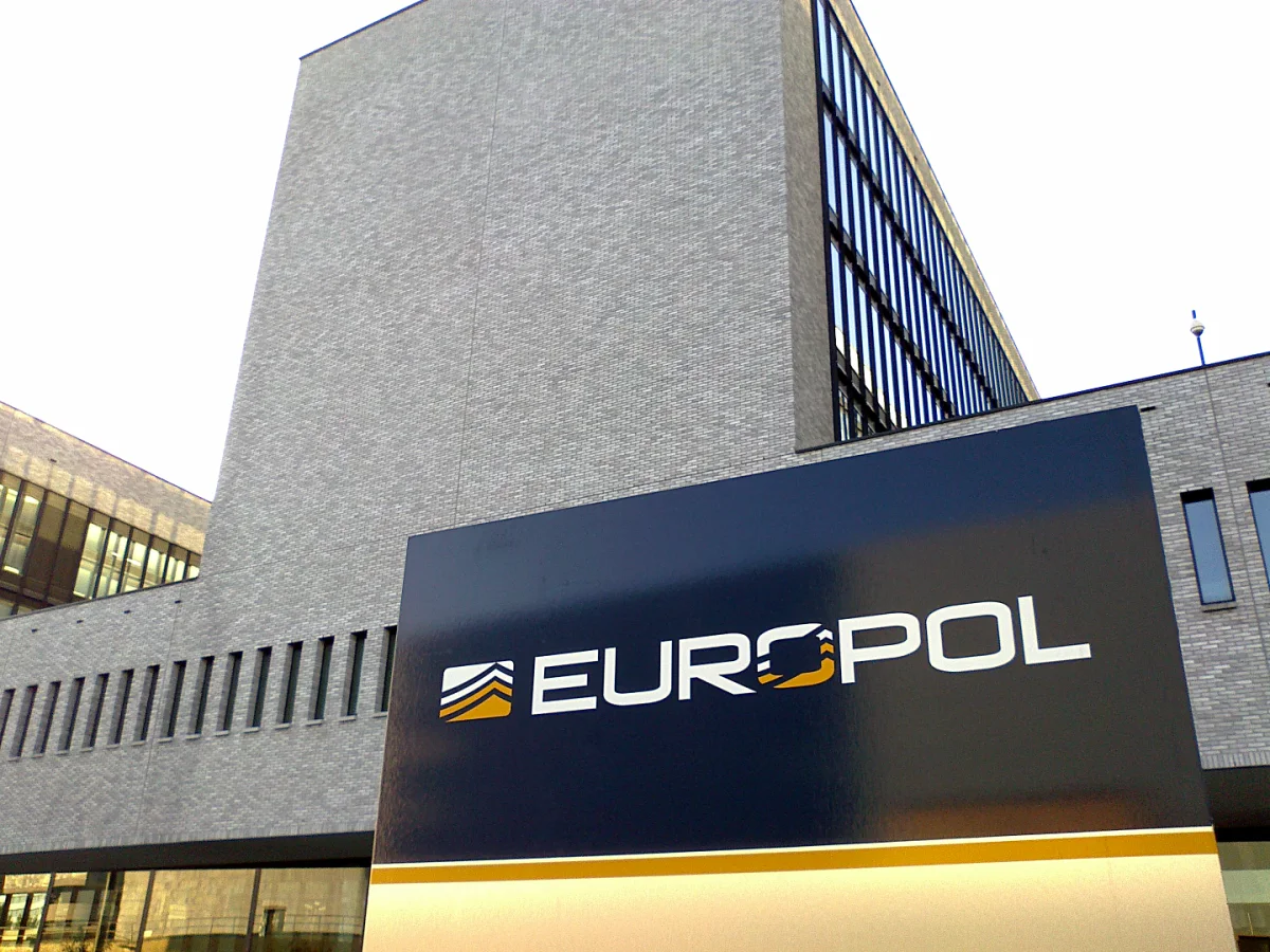 Ein modernes Bürogebäude mit dem Europol-Logo auf einem Schild im Vordergrund. Das Gebäude hat eine nüchterne Architektur.