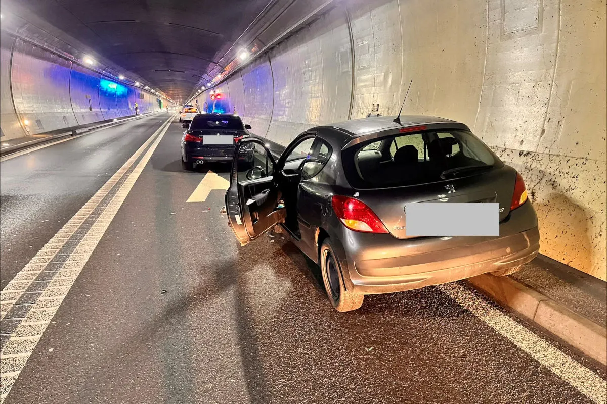 Ein grauer Wagen mit offener Tür steht im Tunnel nahe einem Polizeifahrzeug. Beide Fahrzeuge sind auf der Fahrbahn geparkt.
