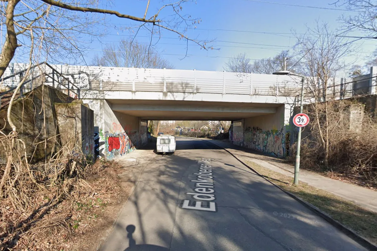 Die Straßenansicht zeigt eine graffitibedeckte Unterführung. Ein kleines Fahrzeug ist auf der Straße sichtbar.