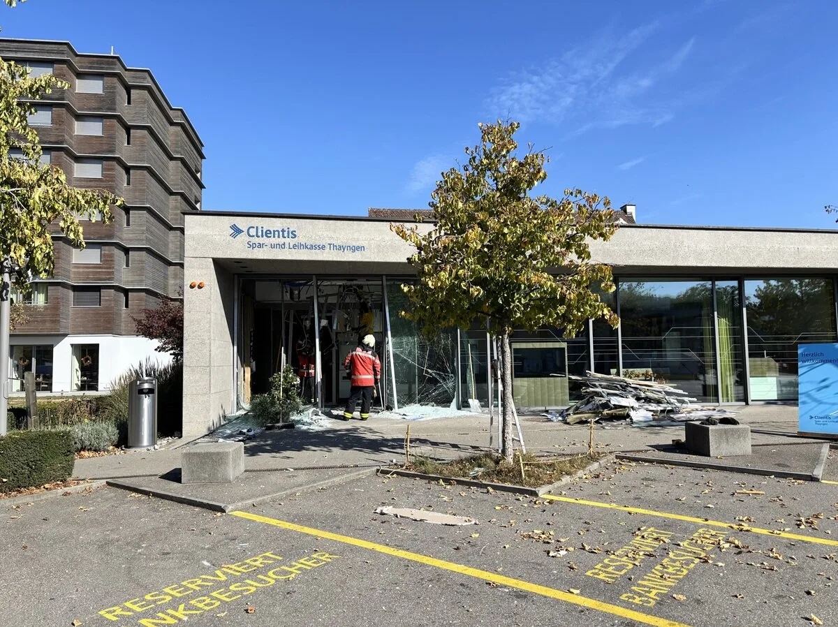 Das Bild zeigt Einsatzkräfte vor einer Bankfiliale. Die Glasfront der Bank ist stark beschädigt, Trümmer sind erkennbar.