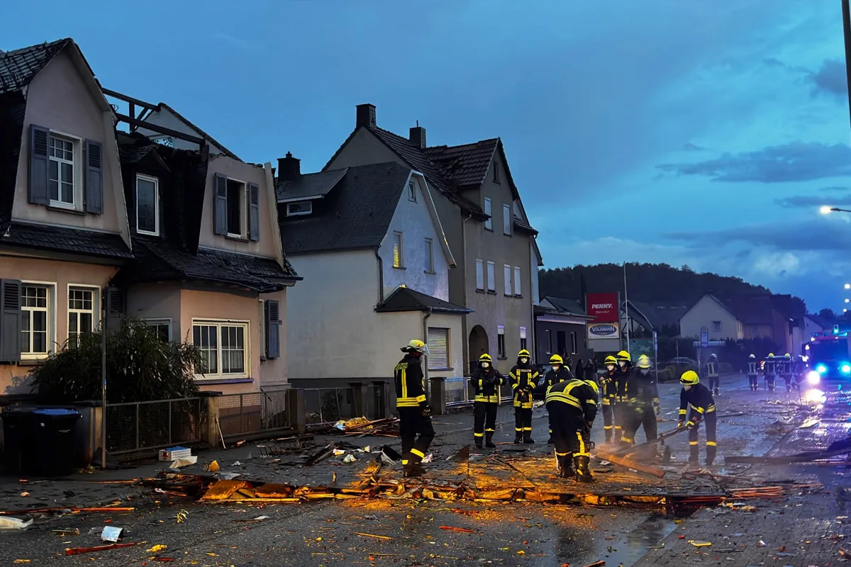 Mehrere Feuerwehrleute in Schutzkleidung entfernen Trümmer von einer Straße. Es ist dunkel, und die Umgebung ist schwach beleuchtet.