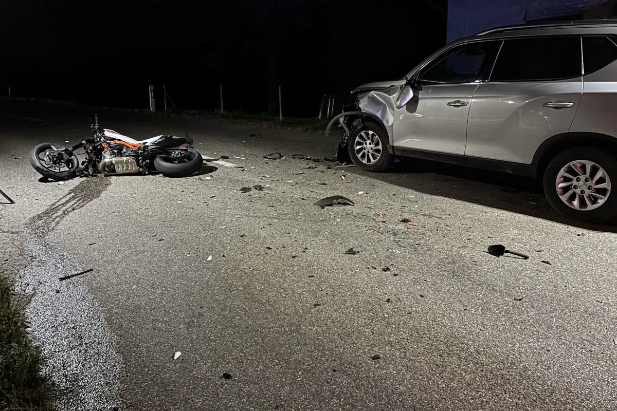 Ein beschädigtes Motorrad liegt auf der Straße neben einem silbernen SUV mit Beifahrerschäden. Der Unfall ereignete sich nachts.