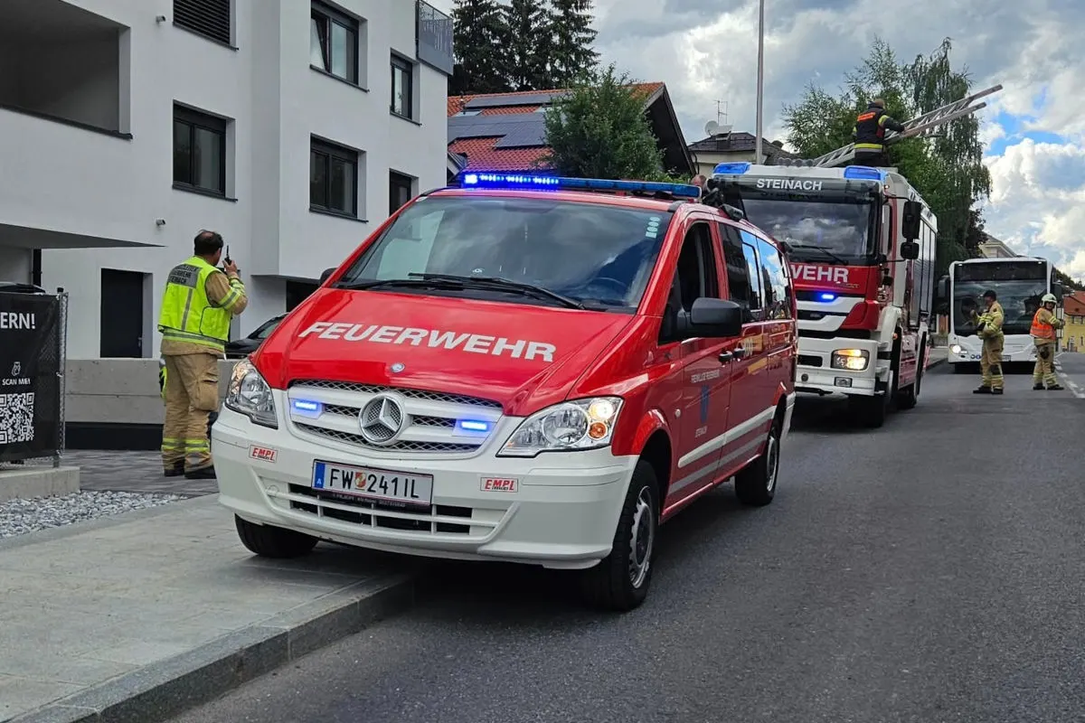 Ein rotes Feuerwehrfahrzeug steht in einer Wohnstraße, begleitet von Einsatzkräften in Uniformen und einem weiteren Feuerwehrwagen.