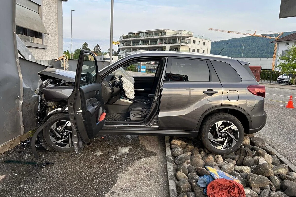 Ein silbernes Auto ist frontal mit einer Hauswand kollidiert. Die Airbags sind ausgelöst, und die Fahrertür steht offen. Es gibt keine sichtbaren Personen.
