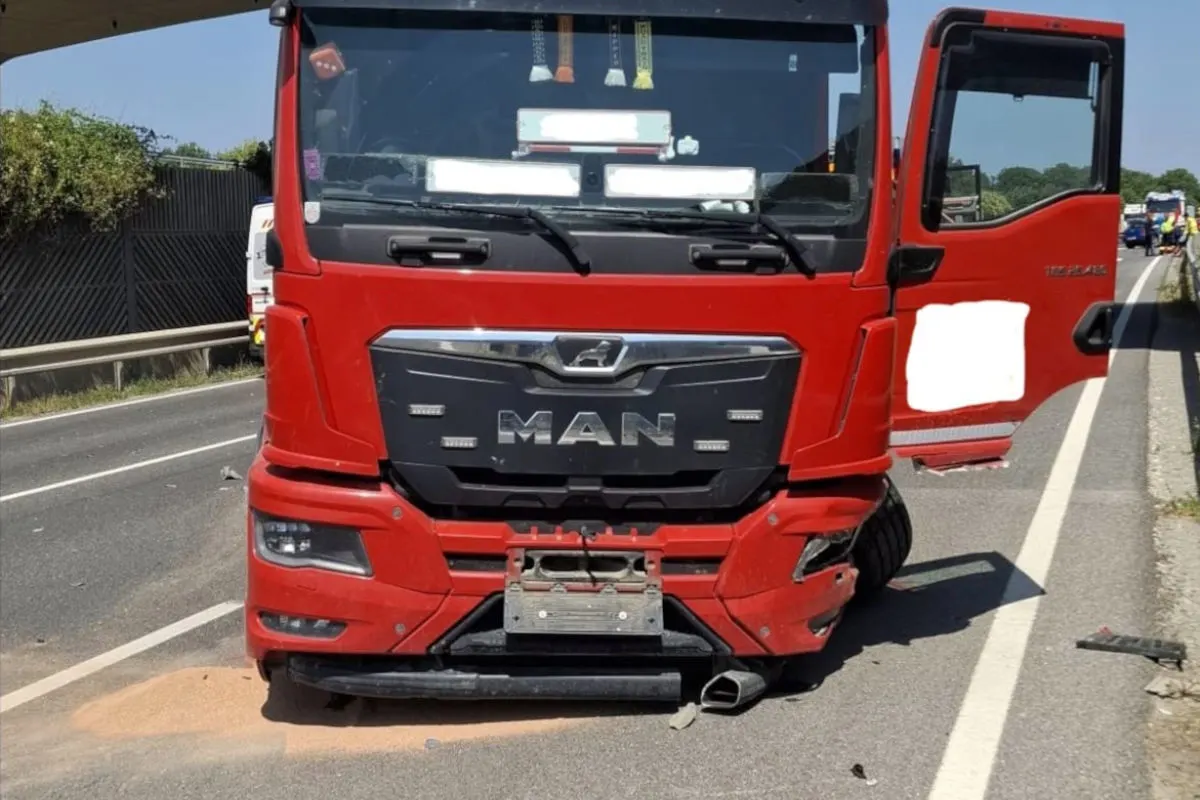 Ein roter MAN-Lkw steht mit beschädigter Front auf einer zweispurigen Straße. Die Umgebung zeigt eine Leitplanke und vereinzelte Fahrzeuge im Hintergrund.
