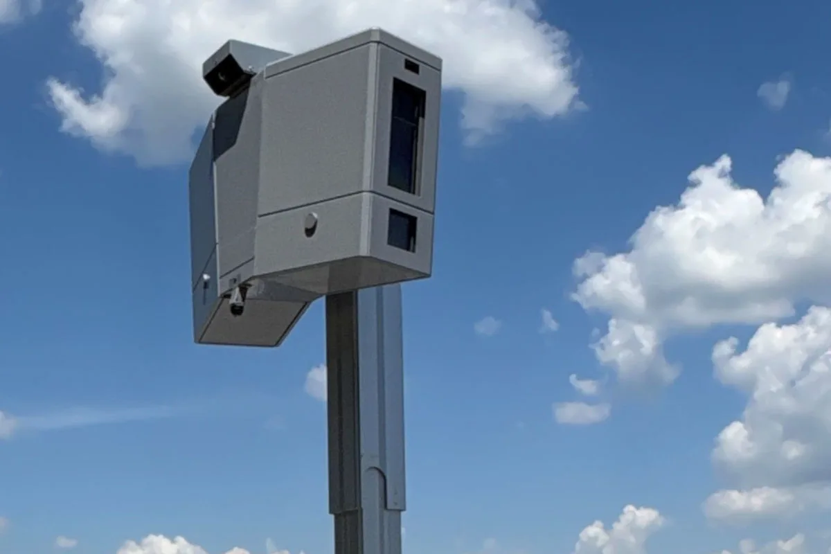 Ein stationärer grauer Blitzer steht vor einem blauen Himmel mit vereinzelten weißen Wolken.