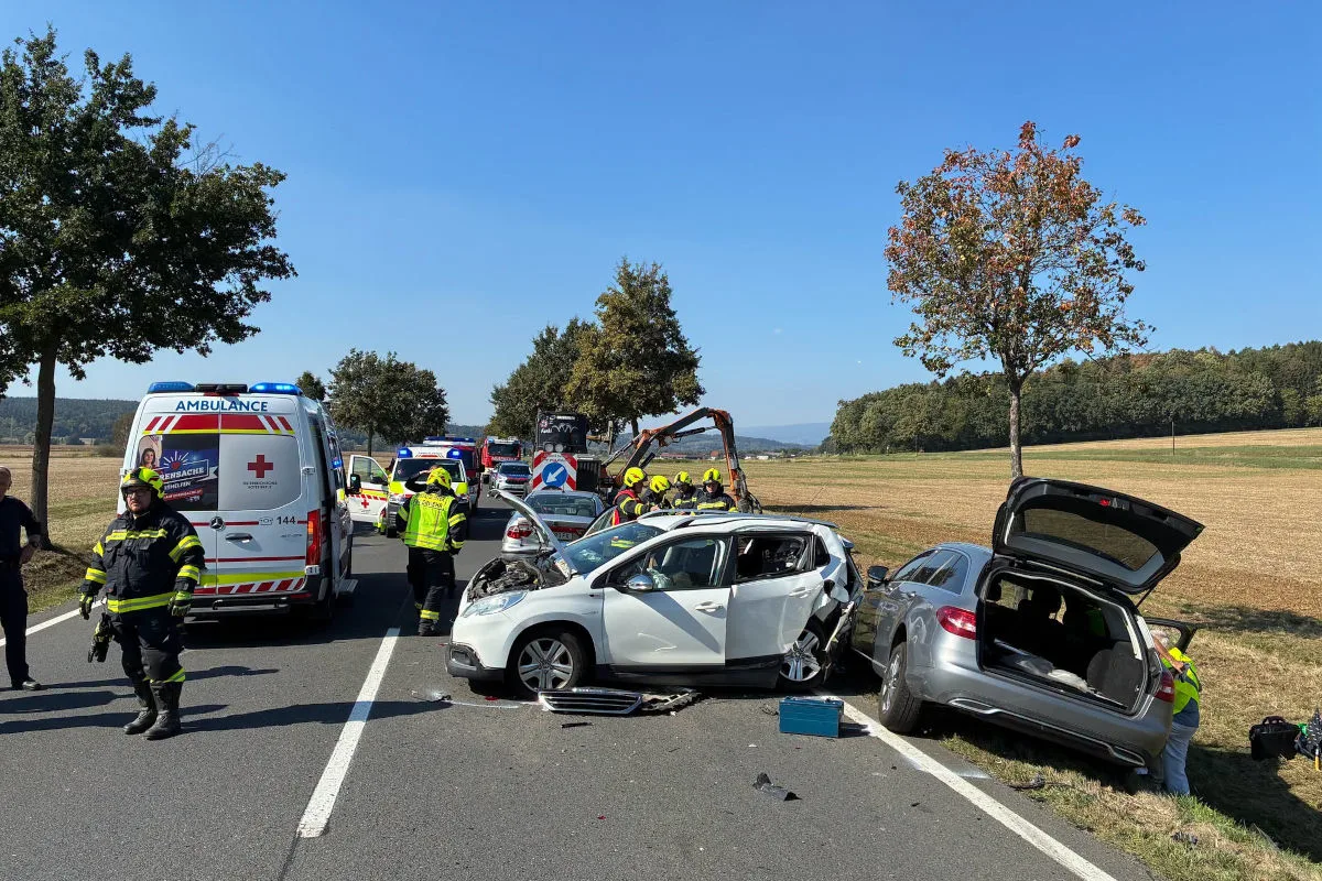 Zwei Autos stehen beschädigt auf einer Landstraße nach einem Unfall, umgeben von Rettungskräften in leuchtender Kleidung. Rettungswagen und Polizei sind im Hintergrund sichtbar.