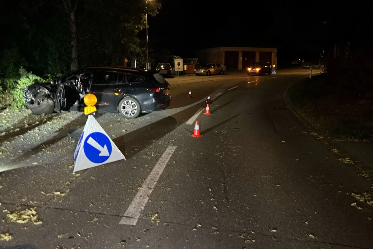 Ein Auto steht nachts mit stark beschädigter Front am Straßenrand, umgeben von Absperrungen und Kegeln.