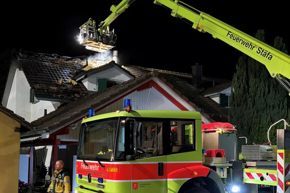 Ein Feuerwehrfahrzeug der Feuerwehr Stäfa steht vor einem Haus mit beschädigtem Dach im nächtlichen Einsatz. Ein Feuerwehrmann ist ebenfalls erkennbar.