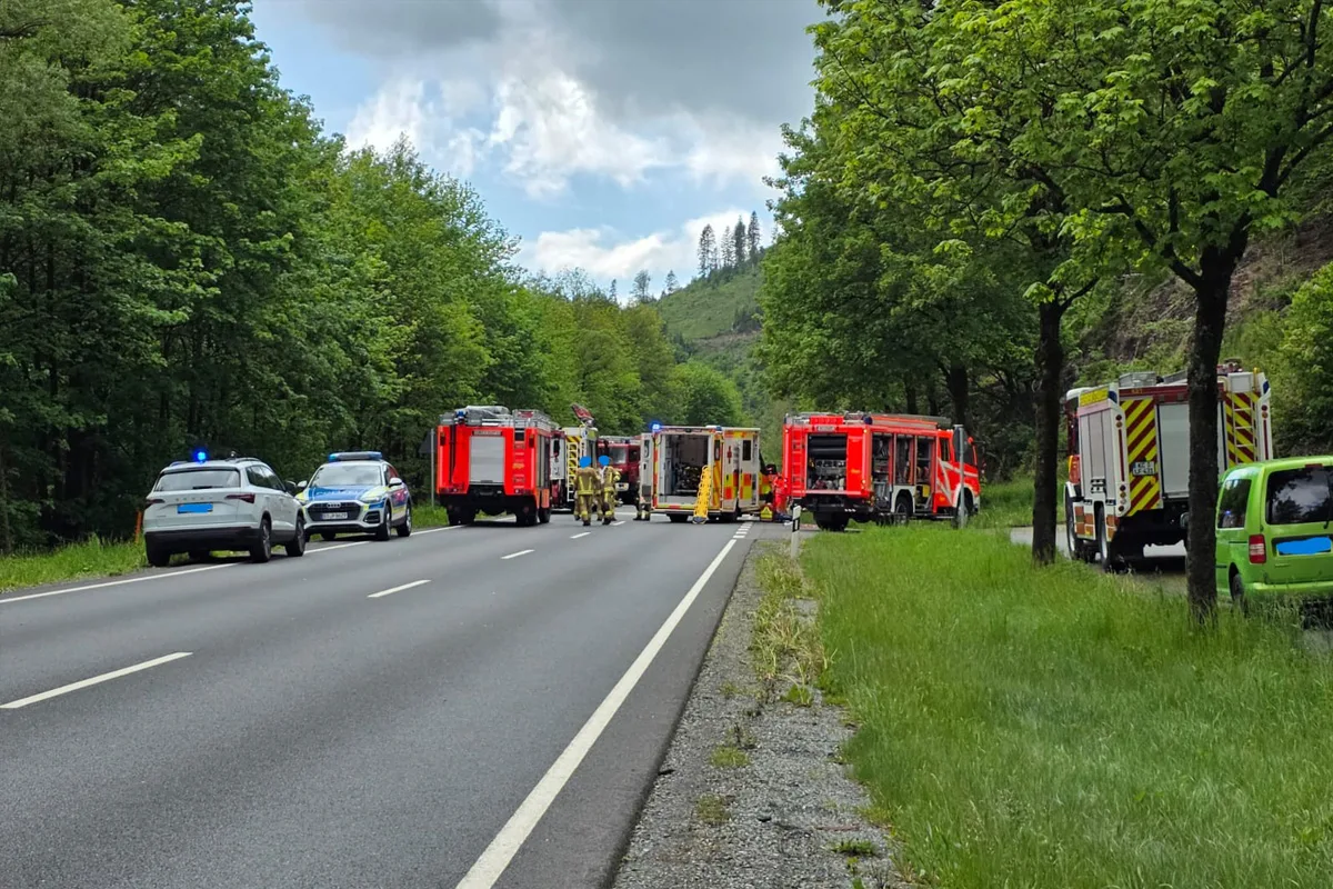 Auf einer Landstraße stehen mehrere Einsatzfahrzeuge, darunter Feuerwehrwagen und Polizeiautos. Die Straße ist von grünen Bäumen umgeben.