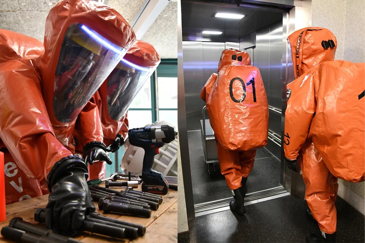 Mehrere Personen tragen orange Schutzanzüge. Links hantieren sie mit Werkzeugen, rechts betreten sie einen Aufzug.