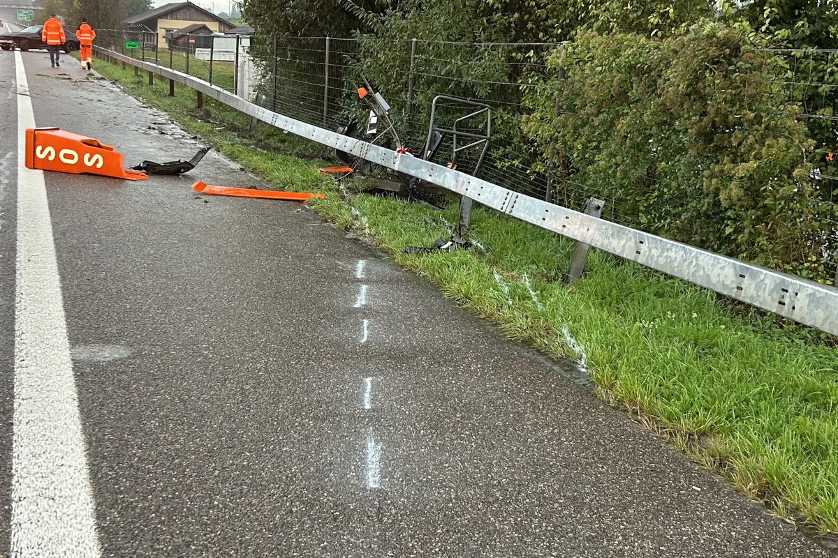 Eine stark beschädigte SOS-Säule liegt neben einer verbogenen Leitplanke an der Autobahn. Auf der nassen Straße sind auch zwei Personen in orangefarbenen Warnwesten zu sehen.