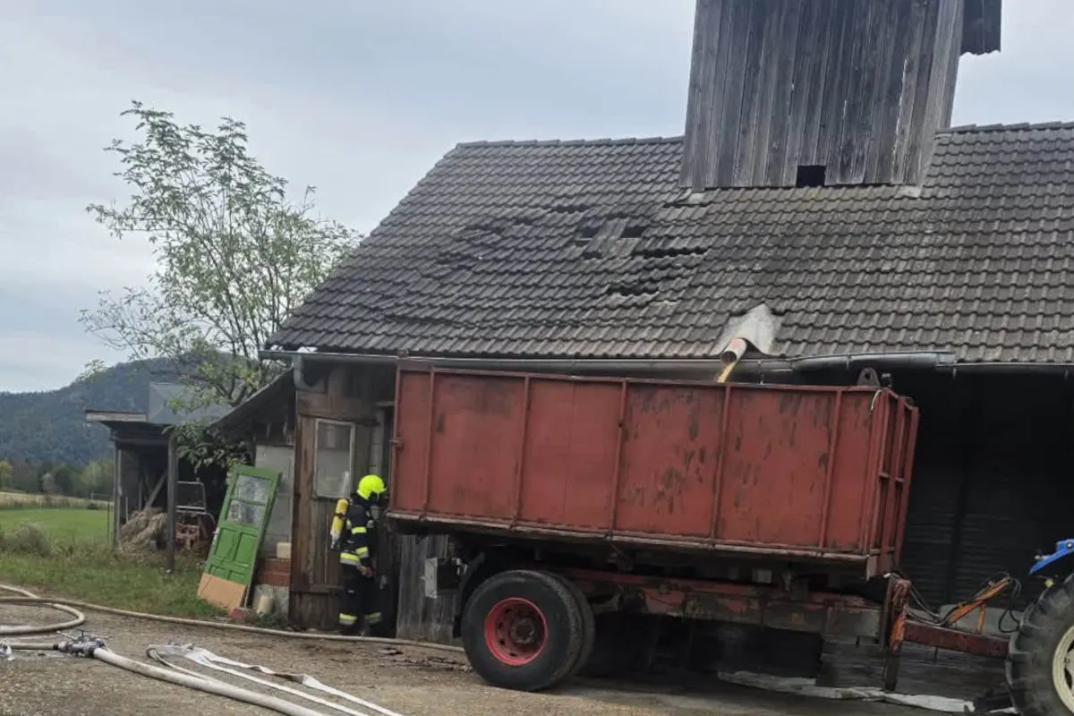 Ein Feuerwehrmann in Schutzkleidung steht vor einem Gebäude mit einem beschädigten Dach, während ein roter Lkw-Anhänger davor geparkt ist.