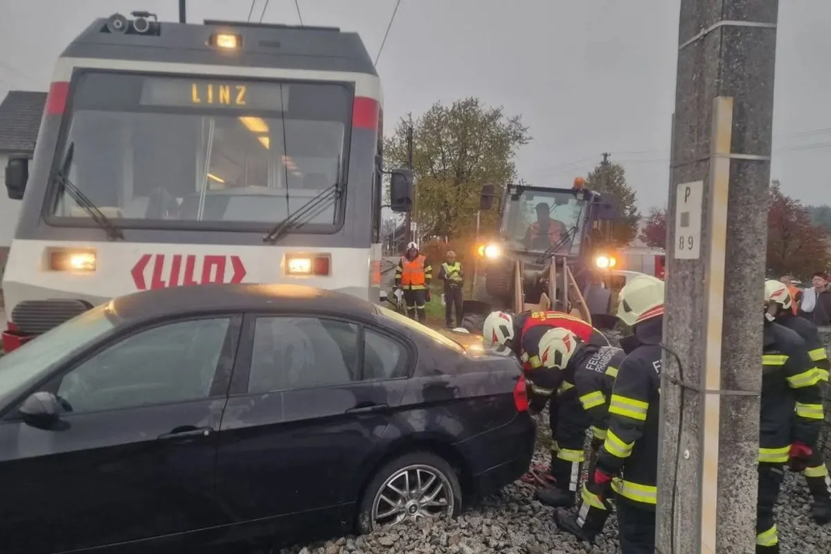 Ein schwarzes Auto steht auf Bahngleisen, nachdem es mit einem Zug zusammengestoßen ist. Feuerwehrleute arbeiten vor Ort.