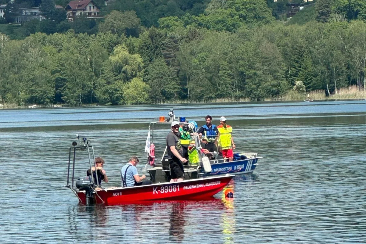 Zwei Boote sind auf einem See zu sehen, besetzt mit Rettungskräften in Einsatzkleidung. Im Hintergrund sind Wälder am Ufer sichtbar.