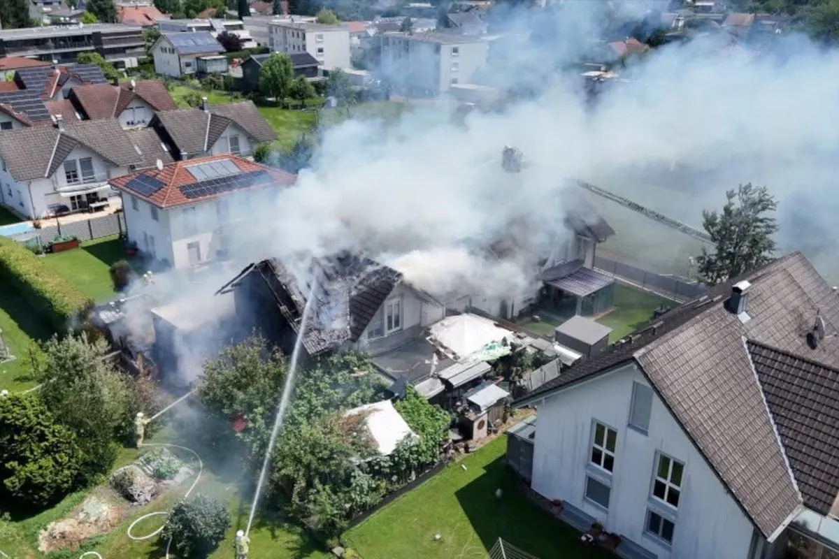 Ein Wohnhaus in einem dicht bebauten Gebiet steht in Flammen. Feuerwehrleute sind dabei, den Brand zu löschen.