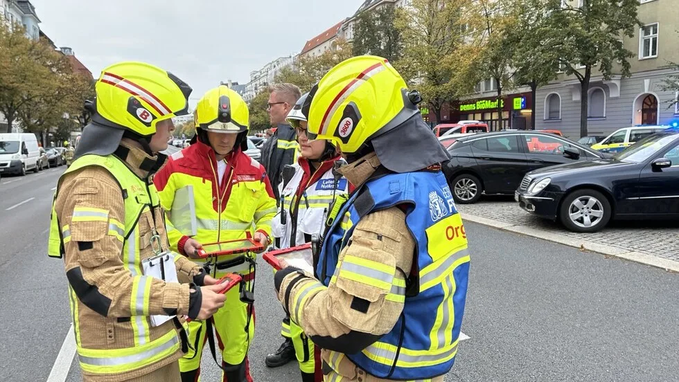 Mehrere Feuerwehrleute in auffälliger Schutzkleidung stehen auf einer Straße und sind in eine Besprechung vertieft.
