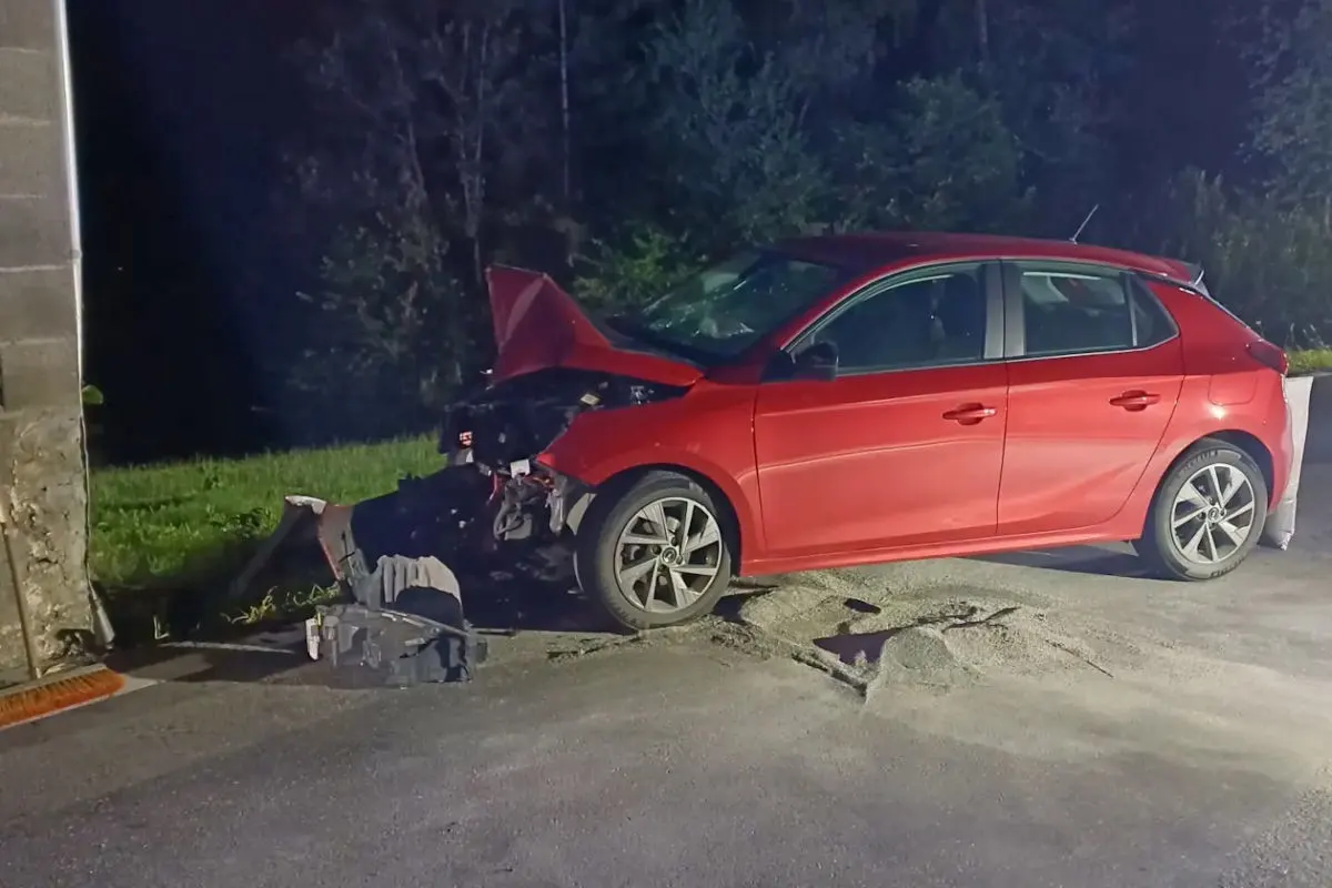 Ein rotes Auto ist bei Nacht mit der Front gegen eine Mauer geprallt. Der vordere Teil des Fahrzeugs ist stark beschädigt.