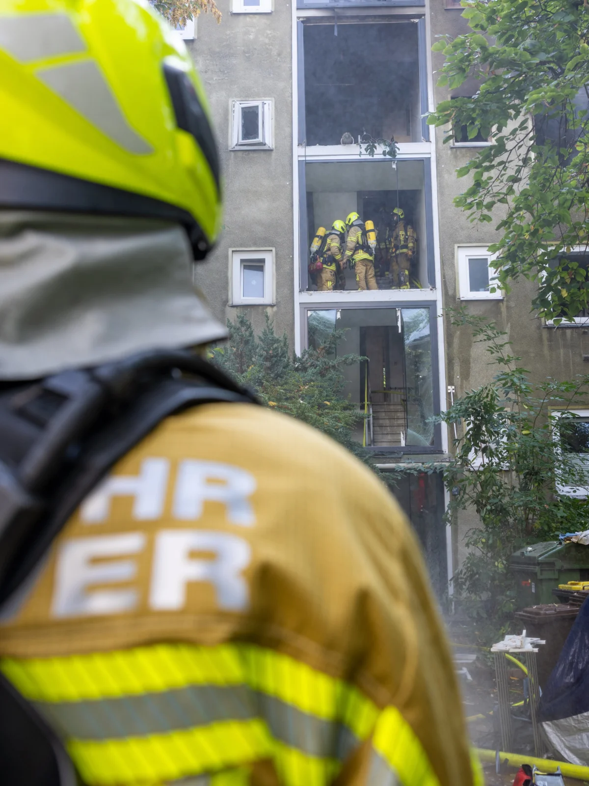 Ein Feuerwehrmann im Vordergrund, während mehrere Kollegen in ein verrauchte Gebäude gehen.