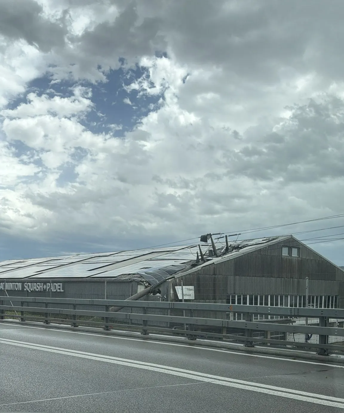 Ein großes Gebäude, vermutlich eine Sporthalle, zeigt erhebliche Sturmschäden. Das Dach ist teilweise eingestürzt, was auf den Sturm zurückzuführen ist.