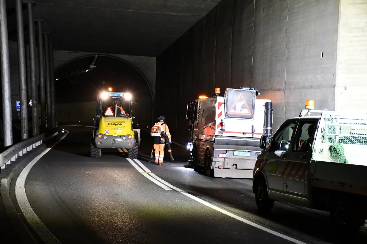 Ein Tunnel bei Nacht mit Straßenbauarbeiten. Zwei Fahrzeuge und ein Arbeiter in Sicherheitskleidung sind sichtbar.