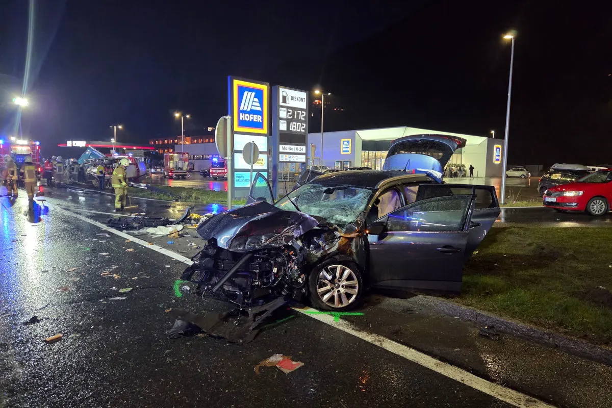 Ein stark beschädigtes Auto steht bei Nacht vor einer Tankstelle. Mehrere Rettungskräfte sind vor Ort und kümmern sich um den Unfall.