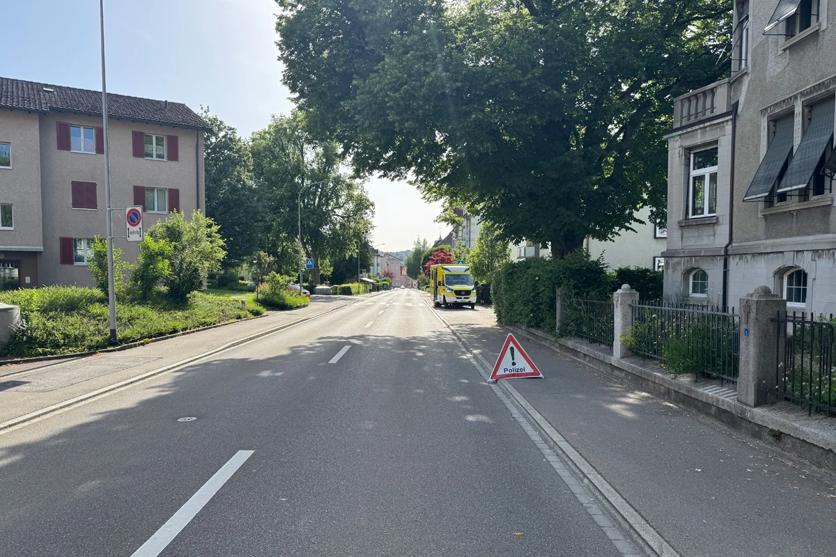 Ein Warnschild mit der Aufschrift 'Polizei' ist am Straßenrand aufgestellt. Ein gelbes Fahrzeug steht weiter vorne geparkt.