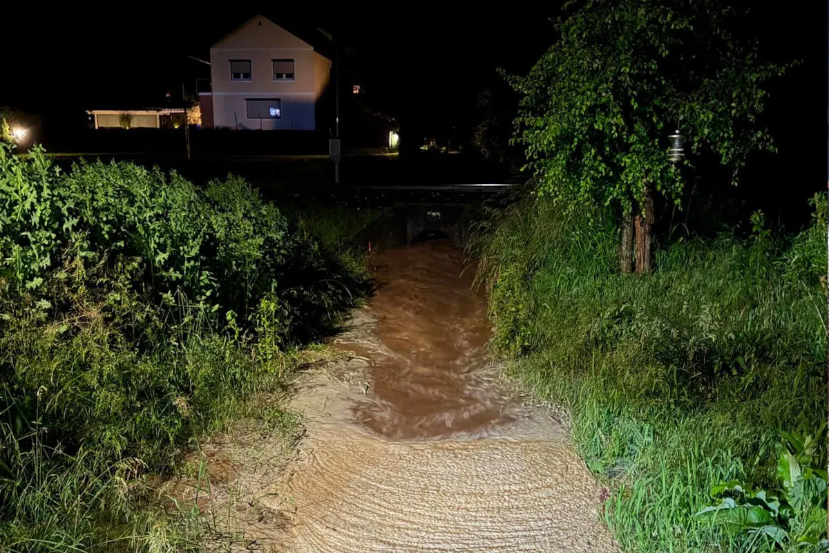 In der Nacht fließt ein stark angeschwollener Bach durch eine grüne ländliche Umgebung. Im Hintergrund steht ein beleuchtetes Wohnhaus.